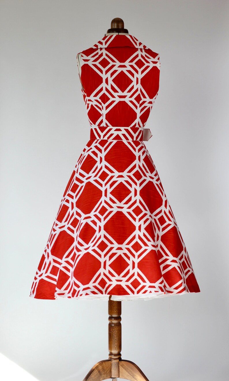 May include: A red and white sleeveless dress with a geometric pattern. The dress has a fitted bodice and a full skirt. The dress is on a mannequin.