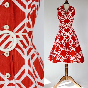 May include: A red and white geometric print dress with a button-up front and a white belt. The dress has a sleeveless design and a flared skirt.