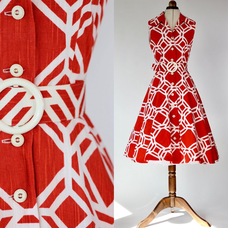 May include: A red and white geometric print dress with a button-up front and a white belt. The dress has a sleeveless design and a flared skirt.