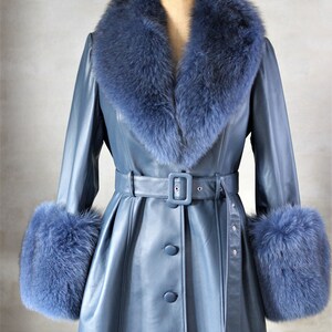 May include: A blue leather coat with a matching fur collar and cuffs. The coat features a belted waist, button-down front, and a classic design. The fur trim adds a touch of luxury to this outerwear piece.