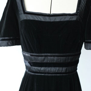 May include: A black velvet dress with a square neckline and short sleeves. The dress has satin trim around the neckline, sleeves, and waist.