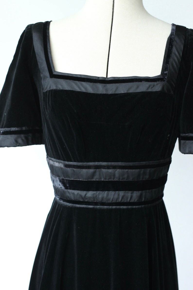 May include: A black velvet dress with a square neckline and short sleeves. The dress has satin trim around the neckline, sleeves, and waist.