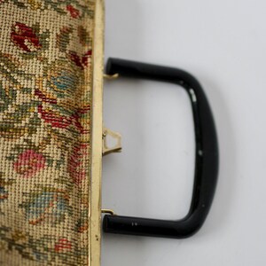 May include: Vintage tapestry handbag with a gold-toned frame and a black handle. The tapestry features a floral design with red, pink, green, and blue hues. The bag has a clasp closure.