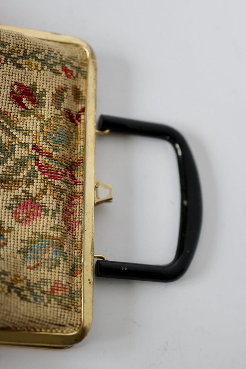 May include: Vintage tapestry handbag with a gold-toned frame and a black handle. The tapestry features a floral design with red, pink, green, and blue hues. The bag has a clasp closure.