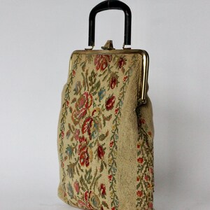 May include: Vintage beige handbag with a black handle and gold-toned clasp. The bag features a floral tapestry design in red, pink, blue, and green. The bag is a classic style, suitable for carrying essentials.