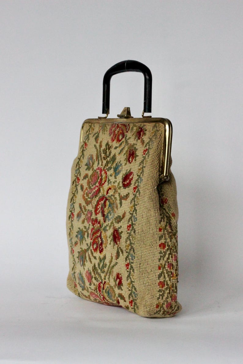 May include: Vintage beige handbag with a black handle and gold-toned clasp. The bag features a floral tapestry design in red, pink, blue, and green. The bag is a classic style, suitable for carrying essentials.