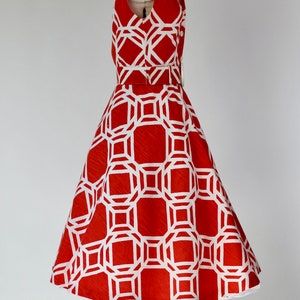 May include: A red and white geometric print dress with a fitted bodice and a full skirt. The dress has a collar and short sleeves.