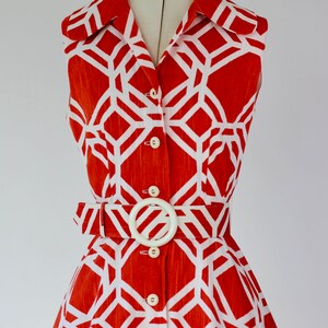 May include: A sleeveless orange and white geometric print dress with a white belt and buttons down the front.
