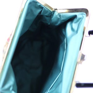 May include: Vintage handbag with a gold-tone frame and a teal satin lining. The bag's interior is visible, showcasing the teal fabric. The exterior features a patterned design with hints of red and pink.