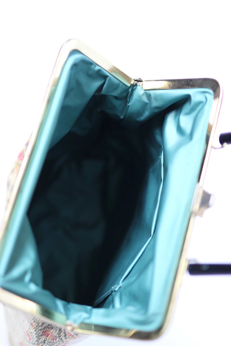 May include: Vintage handbag with a gold-tone frame and a teal satin lining. The bag's interior is visible, showcasing the teal fabric. The exterior features a patterned design with hints of red and pink.