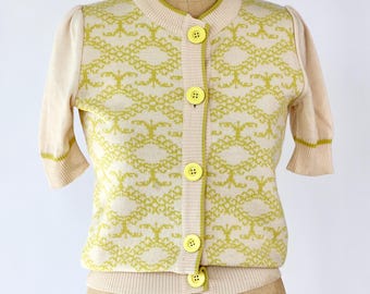 May include: A cream-coloured cardigan with a yellow geometric pattern and yellow buttons. The cardigan has short sleeves and a crew neck.