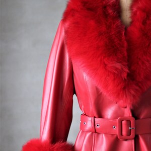 May include: A red leather coat with a large fur collar and cuffs. The coat has a belt and a single button closure.