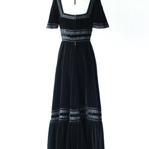 May include: A black velvet maxi dress with a square neckline and short sleeves. The dress features black satin ribbon trim around the neckline, waist, and hem.