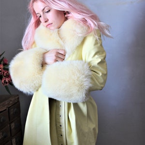 May include: A yellow faux fur coat with a white fur collar and cuffs. The coat is belted and has a long, flowing silhouette.