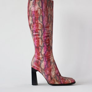 以下が含まれることがあります： ピンクとブラウンのヘビ柄のニーハイブーツ。太いブラックヒールです。