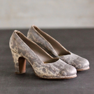 Puede incluir: Un par de zapatos de tacón de piel de serpiente gris con punta.