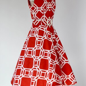 May include: A sleeveless red dress with a white geometric pattern. The dress has a white belt and buttons down the front.