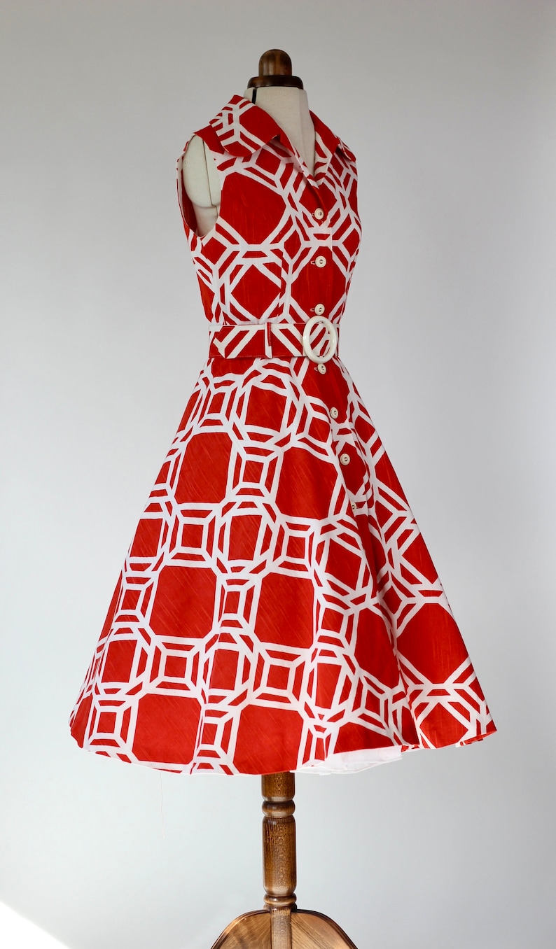 May include: A sleeveless red dress with a white geometric pattern. The dress has a white belt and buttons down the front.