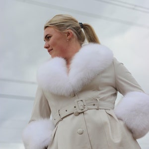 May include: A white faux fur collared coat with a matching fur trim on the cuffs. The coat has a belt and button closure.