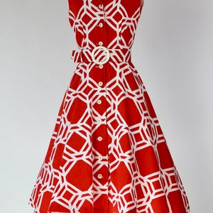 May include: A sleeveless red and white geometric print dress with a white belt and buttons. The dress has a fitted bodice and a full skirt.