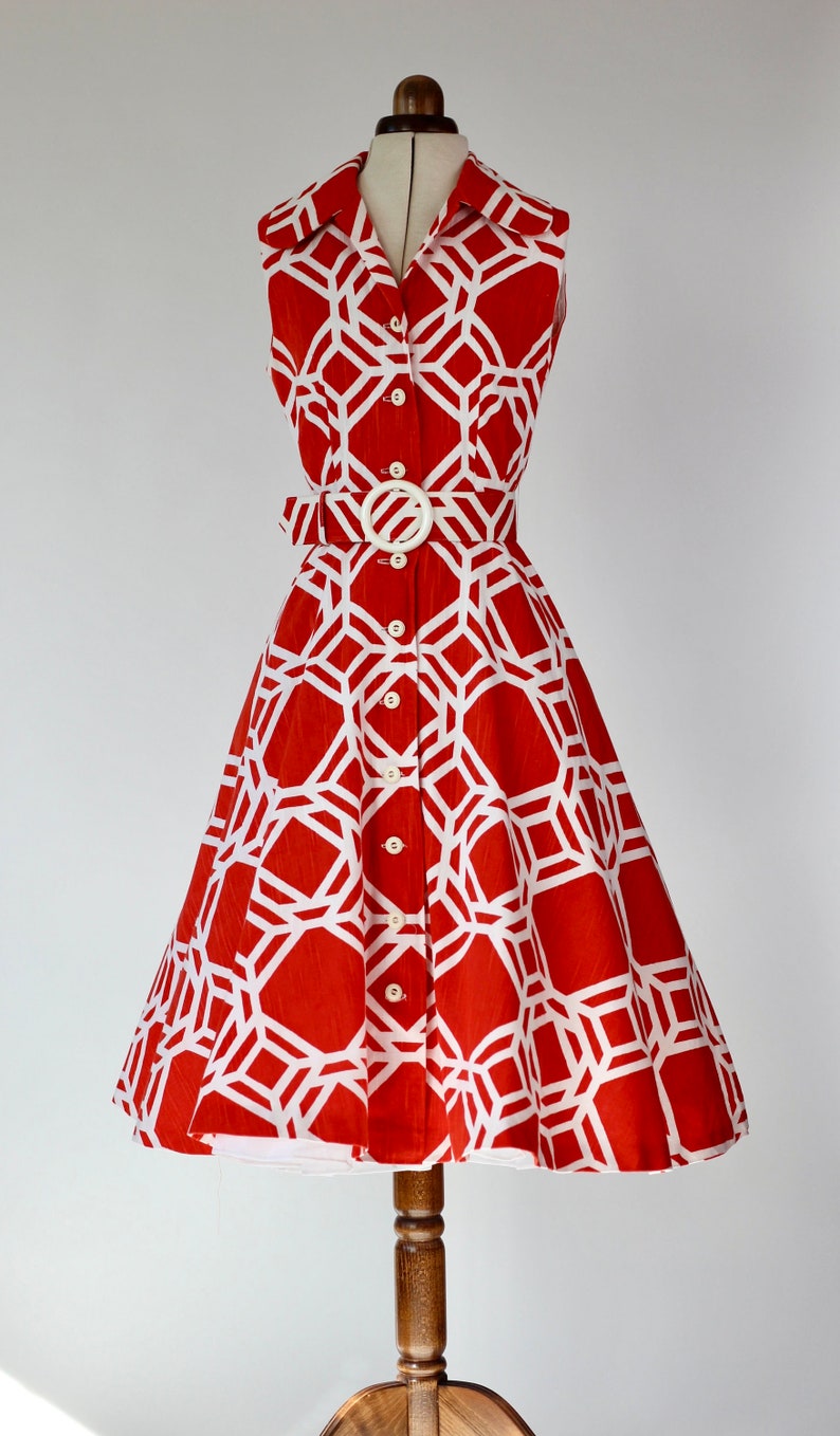 May include: A sleeveless red and white geometric print dress with a white belt and buttons. The dress has a fitted bodice and a full skirt.