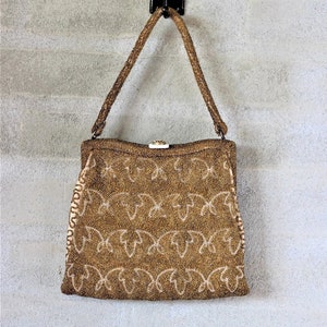 Puede incluir: Un bolso de mano de cuentas doradas con cierre de broche y un delicado patr&oacute;n floral. El bolso tiene una correa larga y est&aacute; colgado de un gancho.