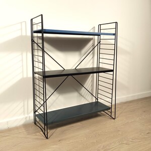 Könnte beinhalten: Ein dreistufiges Bücherregal mit einem schwarzen Metallrahmen und drei Regalböden. Die Regalböden sind in Blau- und Schwarztönen lackiert. Das Design weist eine gitterartige Struktur an den Seiten und abgewinkelte Stützen auf.