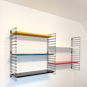 Peut inclure: Étagère murale modulaire avec une structure en métal noir et quatre étagères de couleurs jaune, bleu, blanc et rouge. Les étagères sont rectangulaires. L'ensemble est fixé à un mur blanc, idéal pour le rangement ou l'exposition.