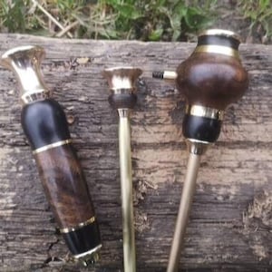 Puede incluir: Tres pipas de fumar de madera con detalles dorados. Las pipas están hechas de madera oscura y tienen un diseño negro y dorado. Las pipas están sobre una superficie de madera.