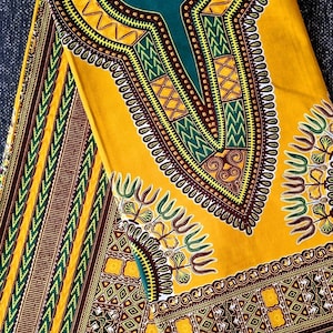 Pode incluir: Tecido amarelo e verde com um padrão geométrico. O tecido tem um design de decote em V com uma borda marrom e amarela.