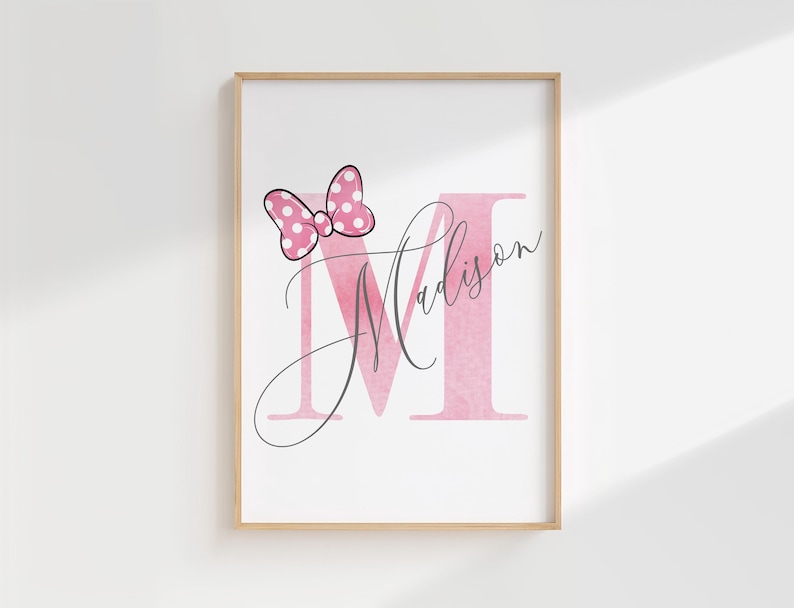 Puede incluir: Impresi&oacute;n enmarcada con una letra 'M' rosa y el nombre 'Madison' en cursiva. Un lazo rosa con lunares blancos est&aacute; encima de la letra. La impresi&oacute;n est&aacute; sobre un fondo blanco.