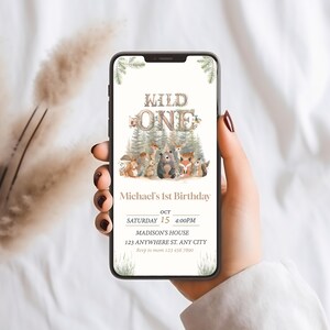 Puede incluir: Una invitación digital para una fiesta de primer cumpleaños con temática de bosque. La invitación presenta un letrero de madera marrón con el texto "Wild One" y un grupo de animales del bosque, incluyendo un zorro, un oso, una ardilla y un ciervo. La invitación también incluye la fecha, la hora y la ubicación de la fiesta.