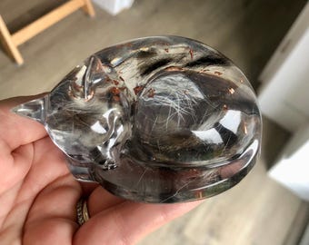 May include: A clear resin sculpture of a sleeping cat with embedded fur and copper flakes.
