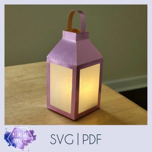 May include: A purple paper lantern with a white paper insert and a light inside. The lantern is sitting on a wooden surface. The text "SVG | PDF" is visible in the image.