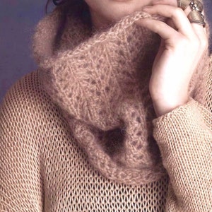 May include: A close-up of a woman wearing a light brown knitted jumper with a matching cowl neck. The jumper has a loose, open weave.