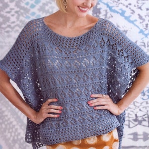 Puede incluir: Una blusa de ganchillo azul claro con un delicado patrón de calado. La blusa tiene un escote redondo y mangas cortas.