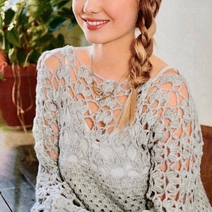 May include: A light grey crochet top with a delicate openwork pattern. The top has long sleeves and a loose fit.