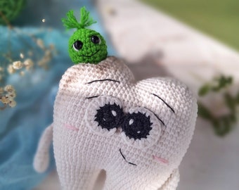 May include: A white crocheted tooth with a smiling face and big black eyes. A small green crocheted creature with a smiling face sits on top of the tooth.