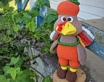 May include: A handmade crochet turkey doll with a brown body, orange pants, and a matching acorn hat. The turkey has a yellow beak, red wattle, and white and colorful tail feathers. It stands on a wooden stump.