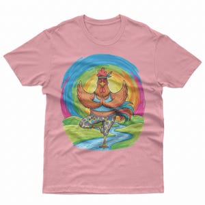 Puede incluir: Una camiseta rosa polvoriento con una ilustración gráfica de un gallo marrón que lleva una camiseta sin mangas azul y leggings estampados mientras realiza una postura de yoga. El gallo lleva una cinta en la cabeza sobre un fondo arcoíris.