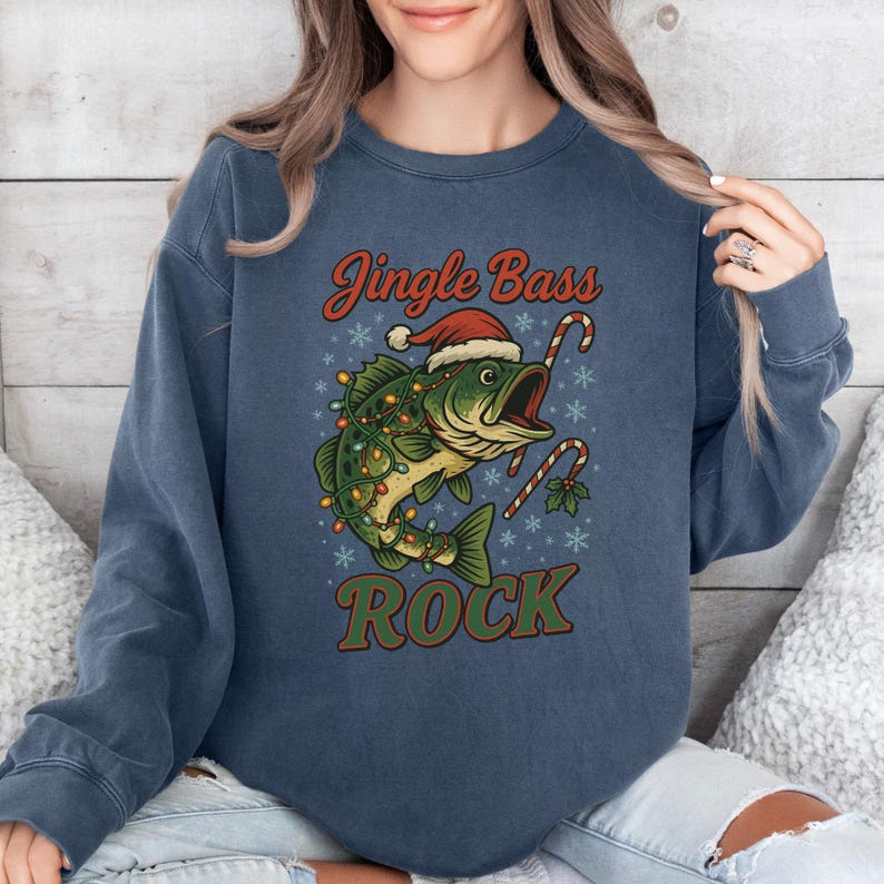 Pu&ograve; includere: Felpa blu navy con grafica a tema natalizio. Il design presenta un pesce con un cappello da Babbo Natale e luci natalizie, con le parole "Jingle Bass Rock" in rosso e verde.