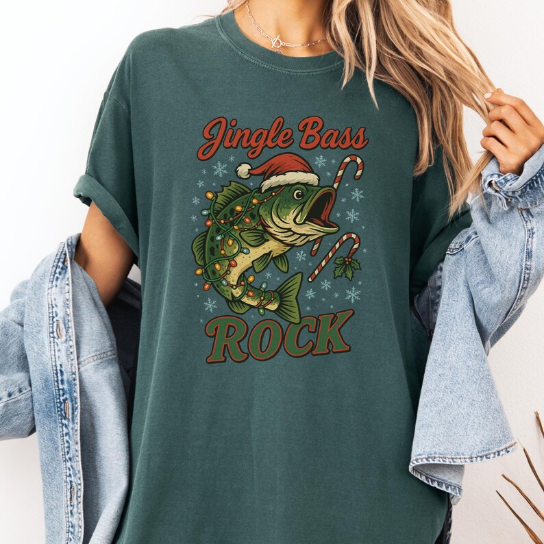Pu&ograve; includere: T-shirt verde scuro con grafica a tema natalizio. La grafica presenta un basso con cappello di Babbo Natale e luci natalizie, con bastoncini di zucchero e le parole "Jingle Bass Rock".
