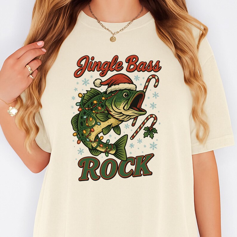 Pu&ograve; includere: T-shirt color crema con grafica natalizia. Presenta un pesce verde con cappello di Babbo Natale e luci natalizie, con le parole "Jingle Bass Rock". Bastoncini di zucchero e fiocchi di neve completano il design festivo.