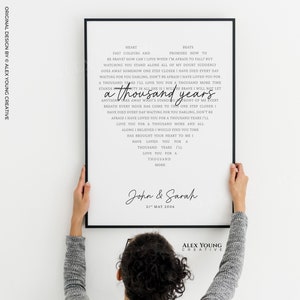 May include: A framed print with a black border, featuring song lyrics in a heart shape. The lyrics include the phrase "a thousand years" in a handwritten font. Below the lyrics are the names "John & Sarah" and the date "21st May 2006".