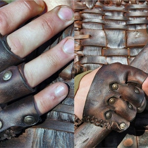 May include: A dark brown leather fingerless glove featuring three individual finger straps secured with metallic brass-toned rivets. The leather has a weathered, textured finish with visible stitching along the wrist edge and embossed lettering.