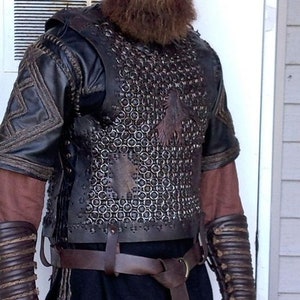 May include: A black leather chest piece featuring a central panel of interlocking metal rings, worn over a dark brown tunic. The armor includes matching leather arm guards with corded detailing, a brown leather belt, and black trousers.