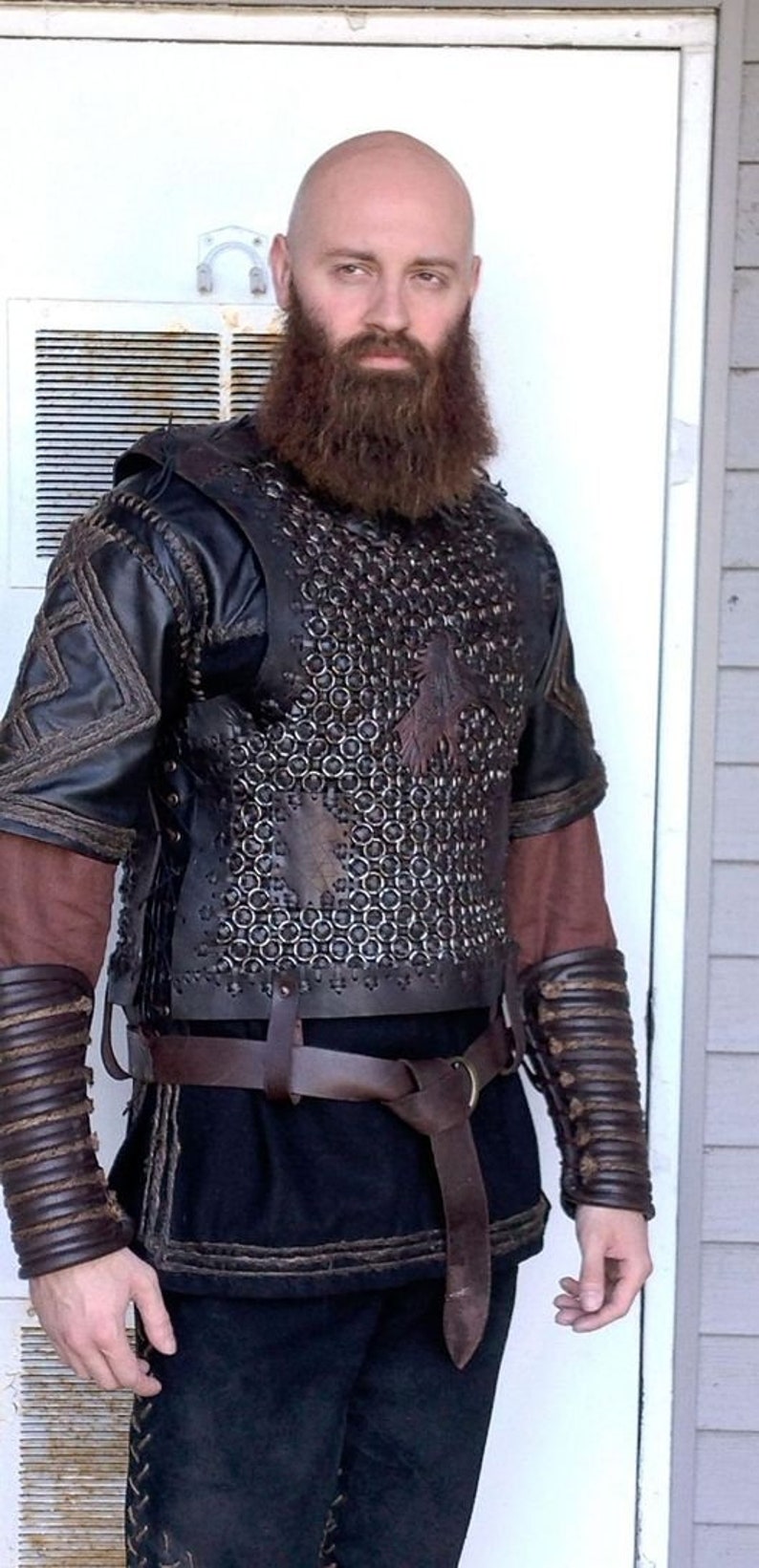 May include: A black leather chest piece featuring a central panel of interlocking metal rings, worn over a dark brown tunic. The armor includes matching leather arm guards with corded detailing, a brown leather belt, and black trousers.