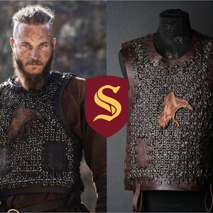 May include: A dark brown leather vest featuring a chainmail-style construction with interconnected metal rings. The vest includes a prominent embossed raven emblem on the chest and leather trim along the edges, displayed on a mannequin form.