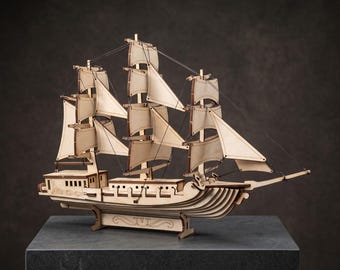 Puede incluir: Un modelo de barco de madera cortado con láser que presenta tres mástiles con velas de color claro y un aparejo intrincado. La embarcación tiene una estructura de casco detallada con niveles de cubierta visibles y un soporte.
