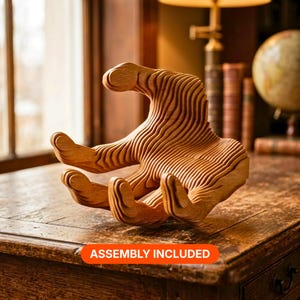 May include: A light brown wooden sculpture shaped like a human hand, constructed from multiple stacked layers of wood that create a topographical, ribbed texture. The object features an open palm and curved fingers. The text ASSEMBLY INCLUDED is visible.
